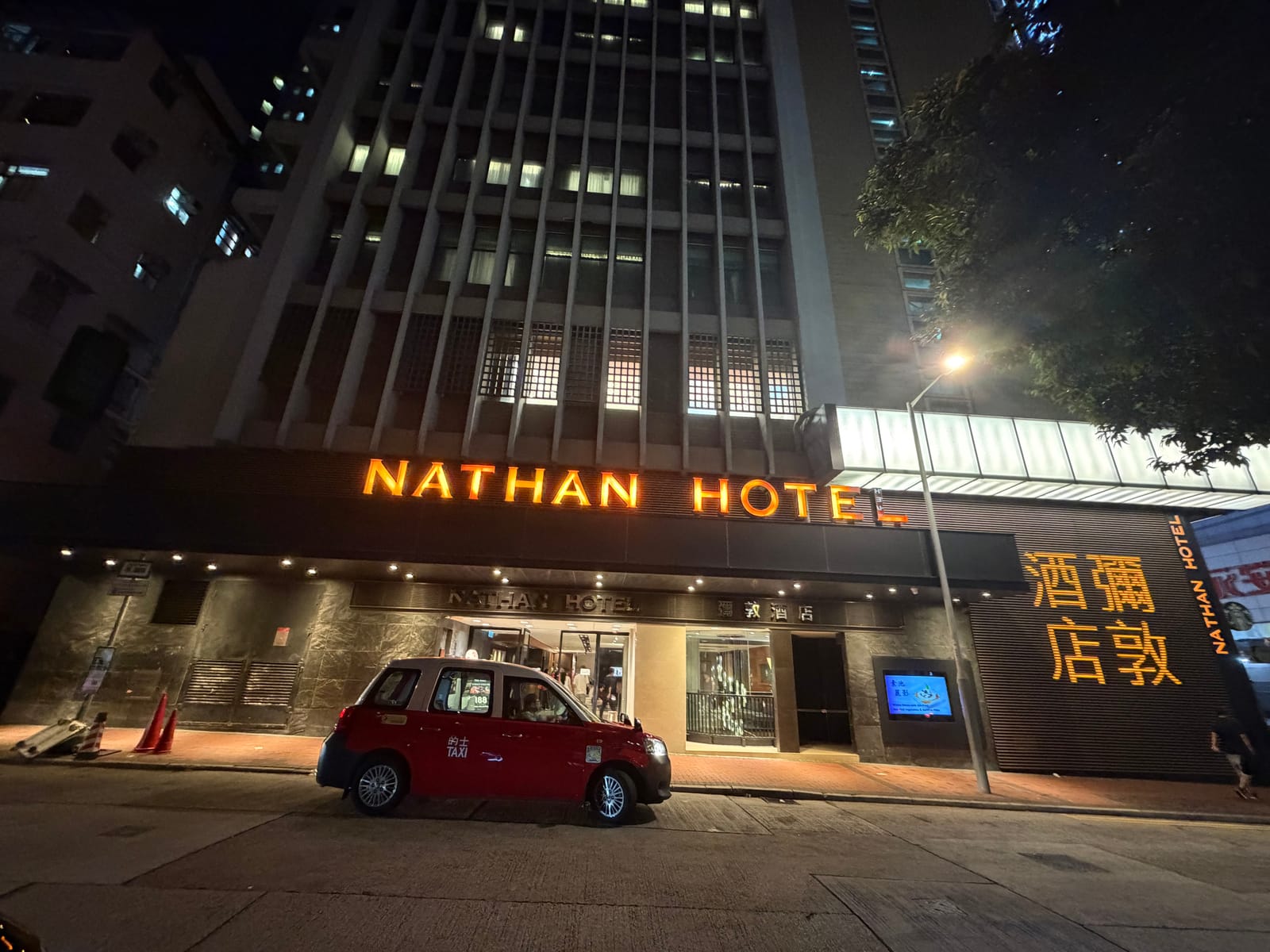 夜の Nathan Hotel。オレンジ色に光る看板と、前に停まる赤いタクシー
